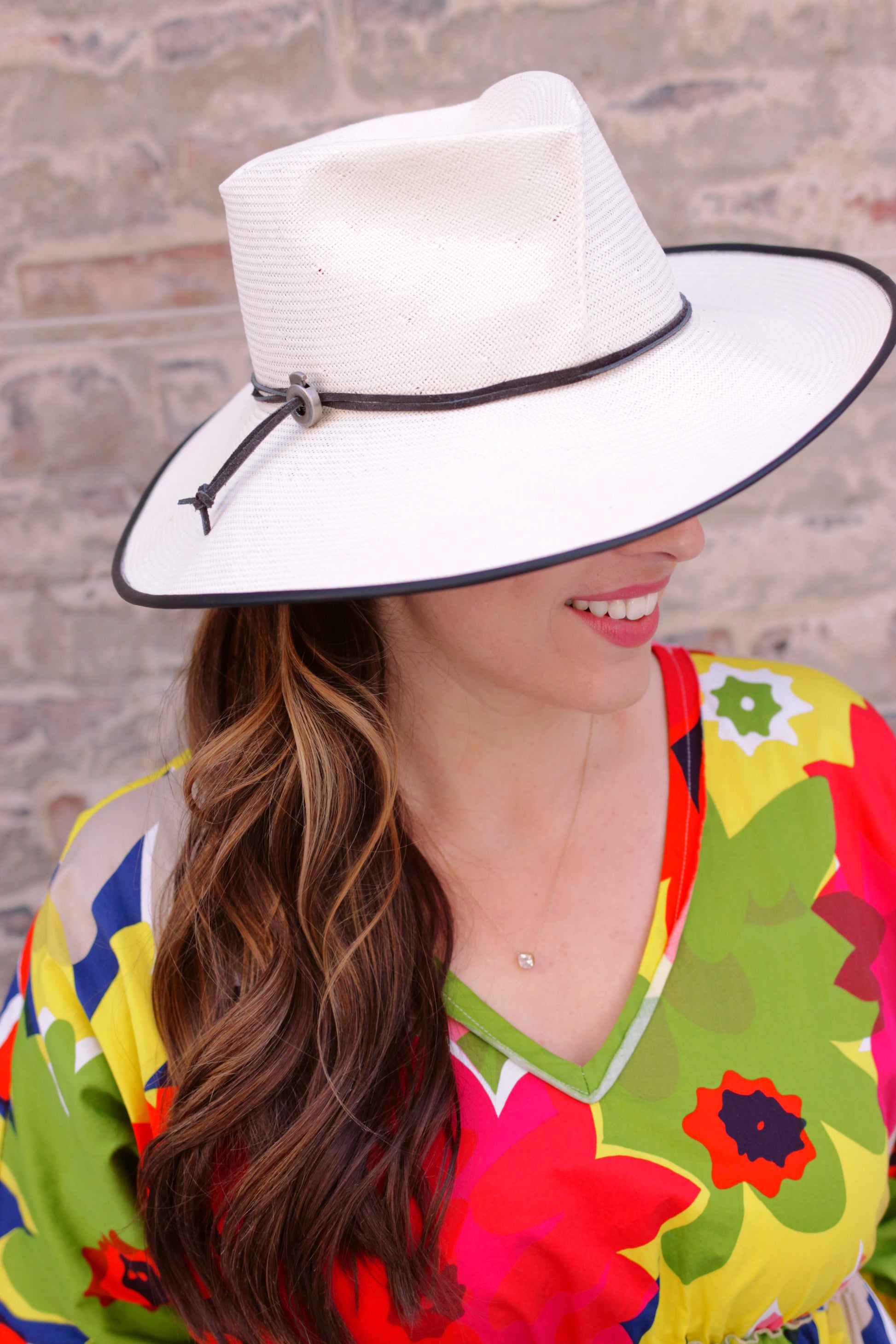 Side view of Ivory straw wide brim fedora on a model. Black piping on the brim with black cord trimThe 